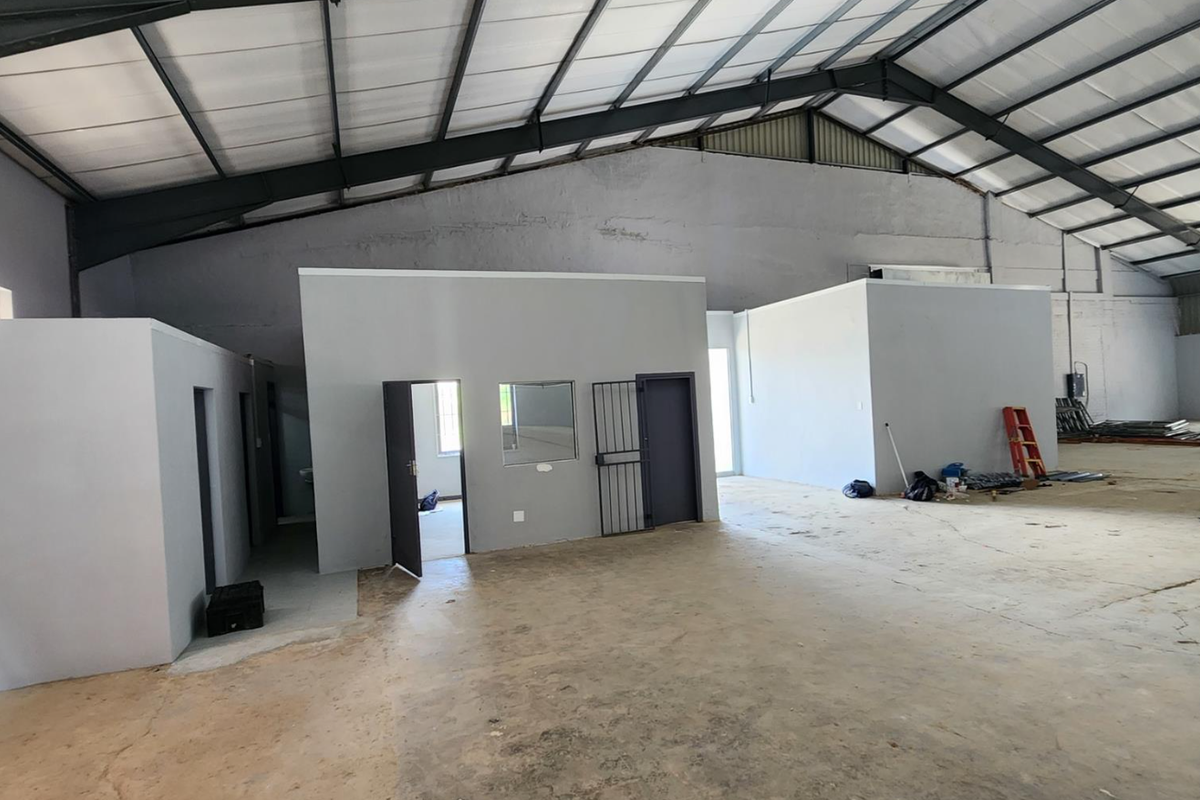 Spacious industrial warehouse featuring high exposed steel roof trusses, concrete flooring, and internal partitioned office spaces with security access.