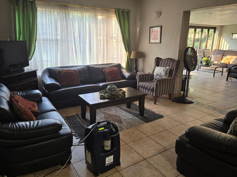 Spacious open-plan living area featuring tiled flooring and large windows, seamlessly connecting to an adjacent sunroom or patio space.