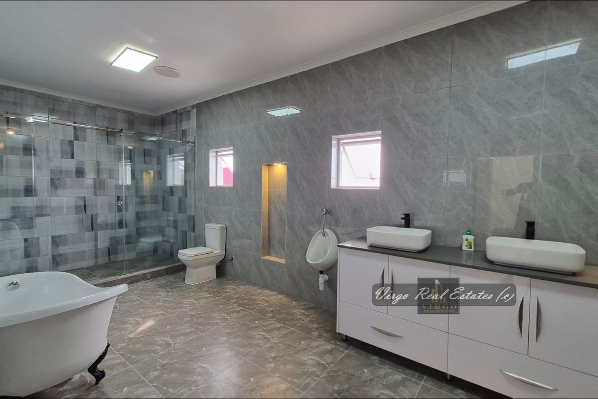 Modern, spacious bathroom featuring a double vanity, freestanding bathtub, glass-enclosed shower, wall-mounted toilet, and a urinal, finished with contemporary grey marble-look tiling.