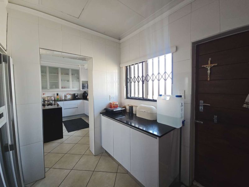 A functional scullery area featuring white built-in cabinetry, dark granite countertops, and tiled finishes, providing additional workspace adjacent to the main kitchen.
