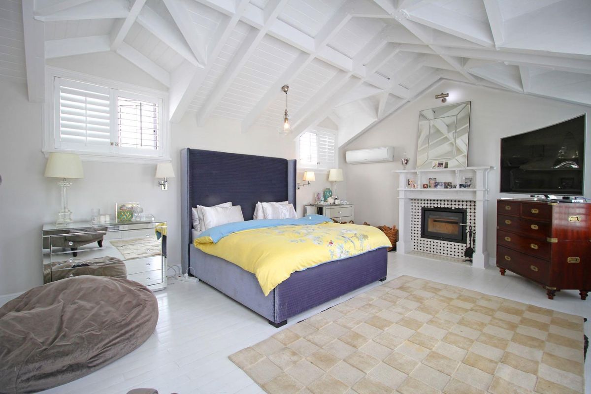 Spacious bedroom featuring a vaulted ceiling with exposed beams, a fireplace with a decorative mantel, and plantation shutters.