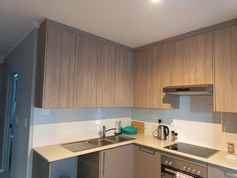 Modern kitchen featuring light wood-grain cabinetry, stone-look countertops, subway tile backsplash, and integrated stainless steel appliances including an oven and hob.