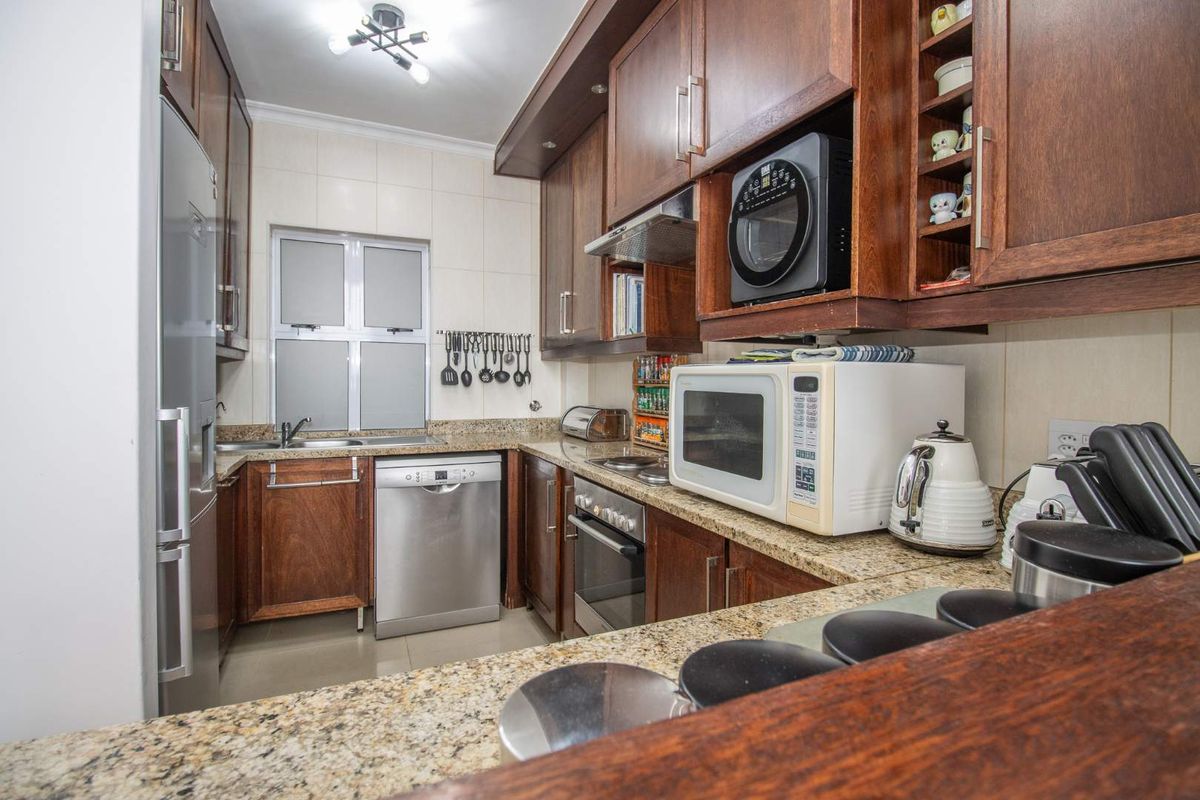 A functional kitchen featuring dark wood cabinetry, granite countertops, integrated oven, extractor fan, and a double sink with tiled splashbacks.