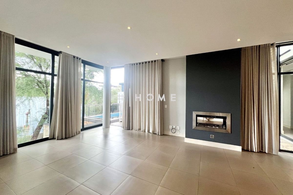 Spacious living area featuring large floor-to-ceiling windows, tiled flooring, and a modern built-in fireplace with a dark feature wall.