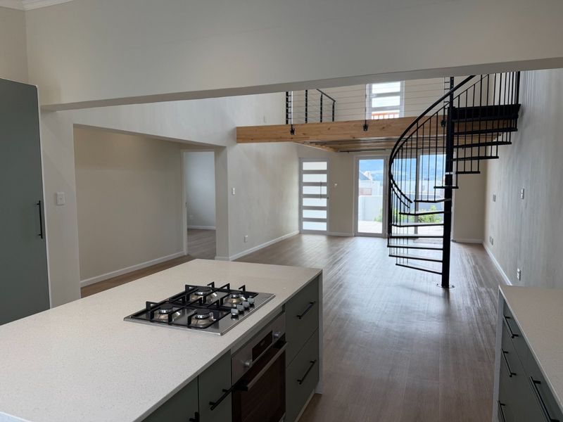Spacious open-plan living area featuring a modern kitchen island with gas hob, timber flooring, and a striking spiral staircase leading to a mezzanine level.