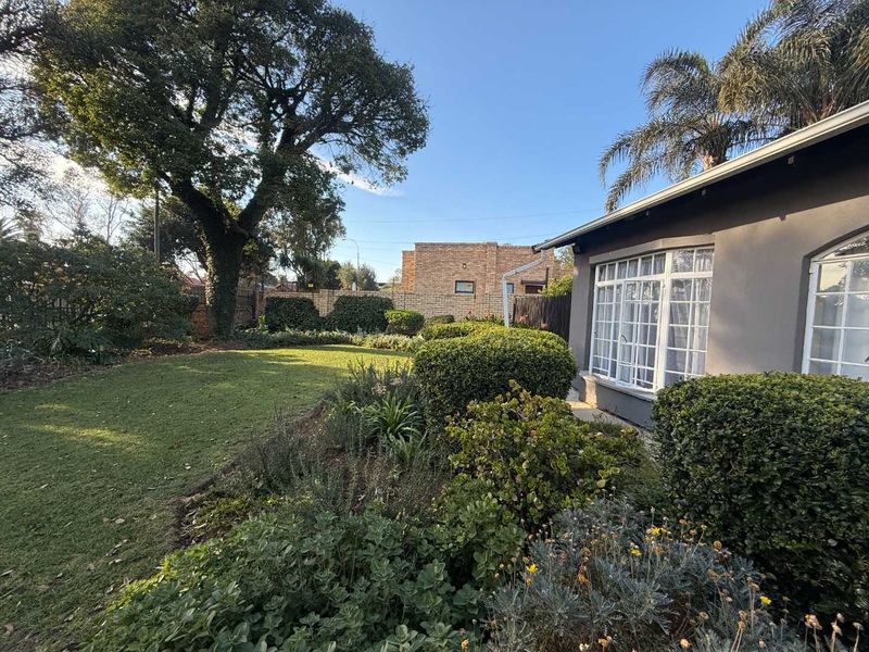 A well-maintained rear garden featuring a lush lawn, established shrubbery, and a brick boundary wall, adjacent to the cottage's exterior facade.