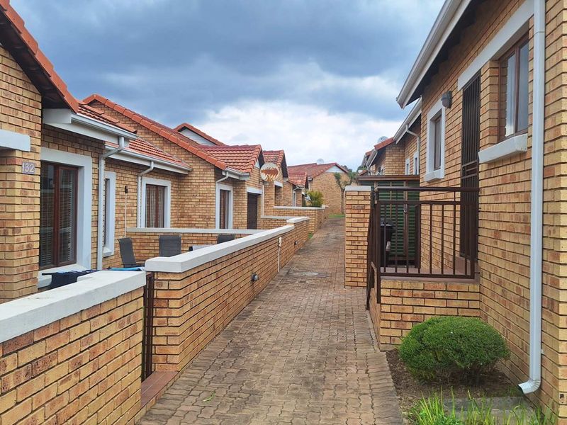 A view of the exterior rear walkway featuring face brick apartment units with tiled roofs and paved pathways.