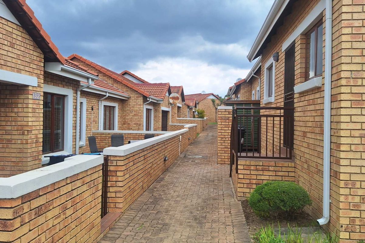 A view of the exterior rear walkway featuring face brick apartment units with tiled roofs and paved pathways.