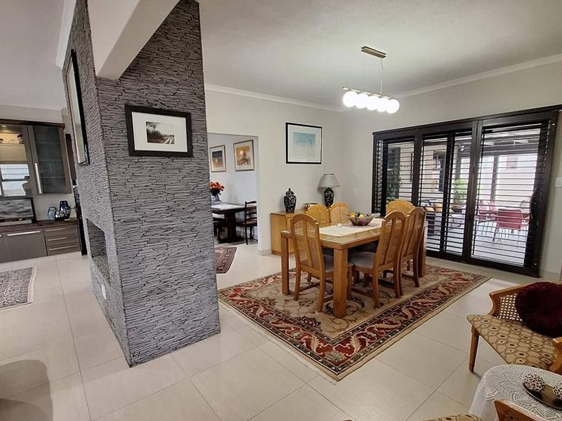 Spacious open-plan living and dining area featuring a striking stone-clad feature wall, large format floor tiles, and seamless access to the outdoor patio.