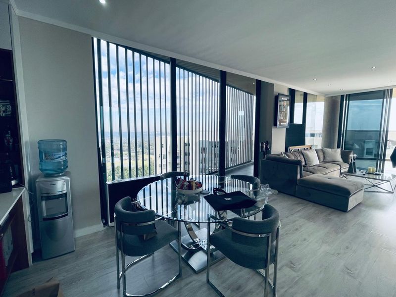Modern open-plan living and dining area featuring floor-to-ceiling windows with vertical louvres, recessed lighting, and light-toned laminate flooring.