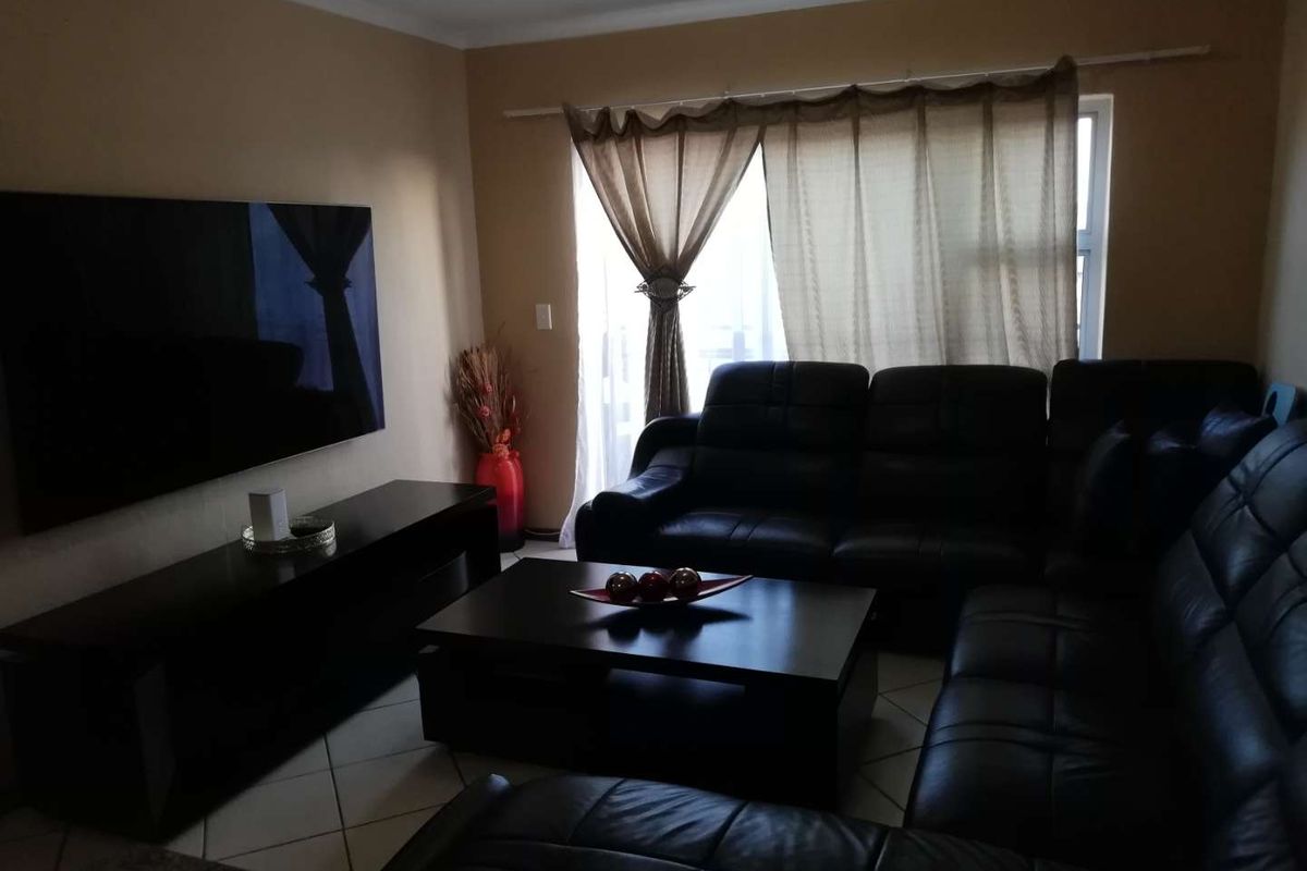 A comfortable living room featuring tiled flooring and a large window with curtains, providing a functional space for relaxation.