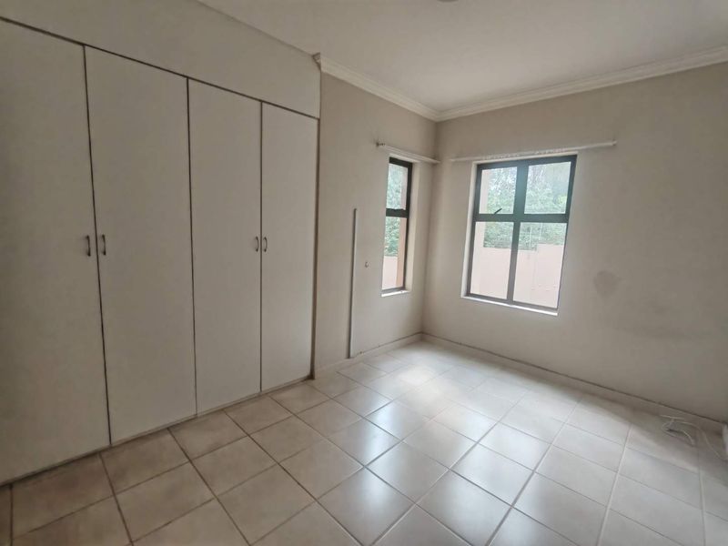 A bright, empty bedroom featuring built-in cupboards, tiled flooring, and large windows, offering a clean canvas for personalization.