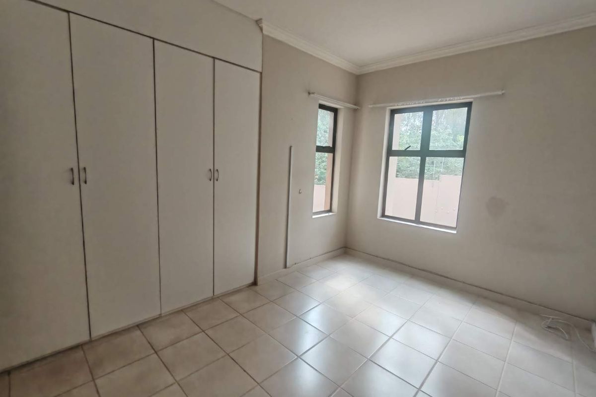 A bright, empty bedroom featuring built-in cupboards, tiled flooring, and large windows, offering a clean canvas for personalization.