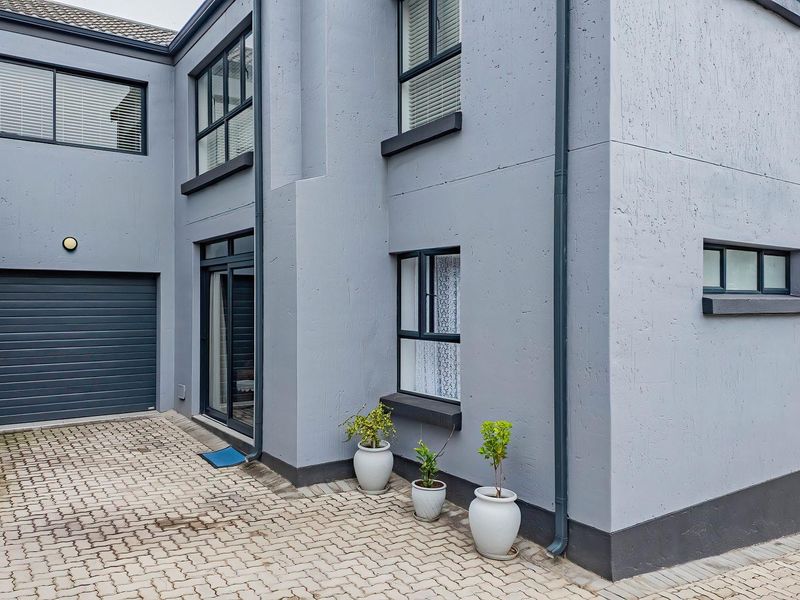 A modern exterior view of an apartment building featuring a paved driveway, integrated garage, and grey rendered facade with dark window frames.