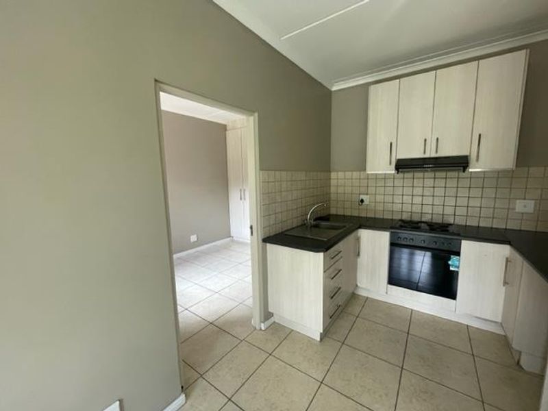 A functional kitchen featuring light-toned cabinetry, a tiled backsplash, built-in oven, and gas hob, with an adjacent view into a bedroom area.