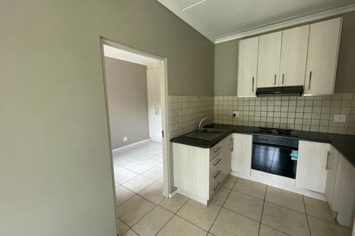 A functional kitchen featuring light-toned cabinetry, a tiled backsplash, built-in oven, and gas hob, with an adjacent view into a bedroom area.