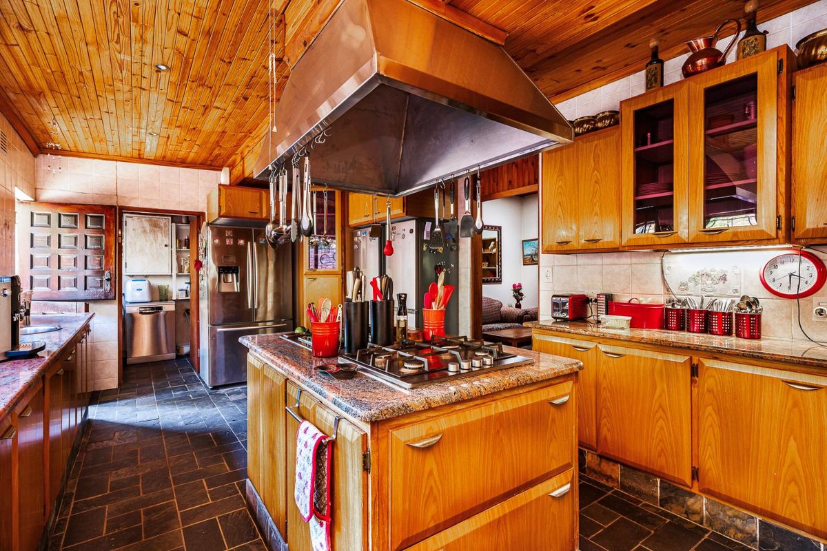 A spacious kitchen featuring timber ceilings, slate flooring, granite countertops, and a central island with a built-in gas hob and stainless steel extractor.