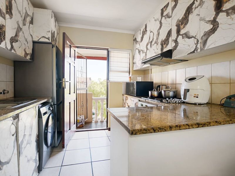 Compact kitchen featuring marble-patterned cabinetry, granite countertops, tiled flooring, and direct access to a balcony area.