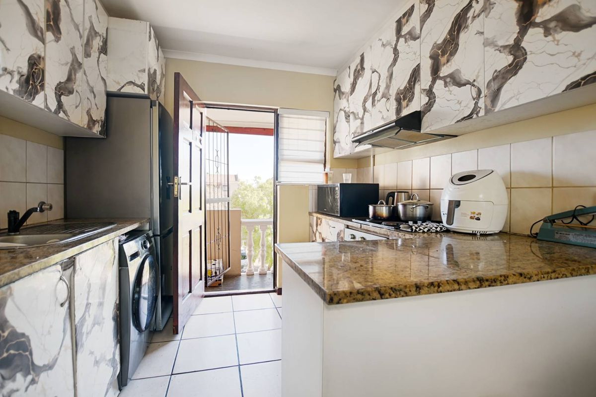 Compact kitchen featuring marble-patterned cabinetry, granite countertops, tiled flooring, and direct access to a balcony area.