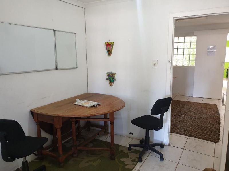 A functional office space featuring tiled flooring, a wall-mounted whiteboard, and a doorway leading to an adjacent room with glass block windows.