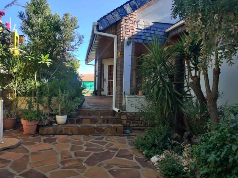 A rear exterior view featuring a stone-paved patio area leading to a brick-clad house facade with tiled roofing and established garden surroundings.