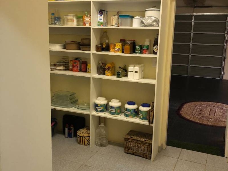 A functional pantry or scullery area featuring built-in white shelving units and tiled flooring, providing ample storage space adjacent to the garage.
