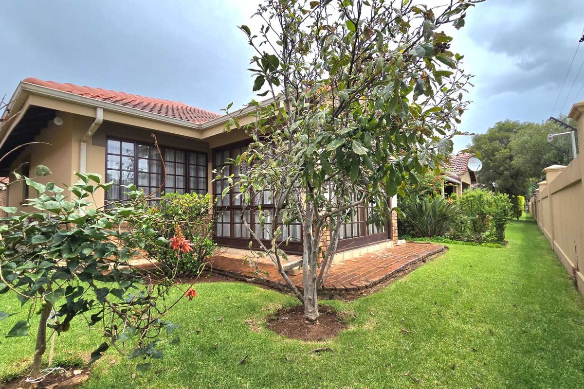 Rear view of the property featuring a brick patio, established garden, and perimeter wall with electric fencing.