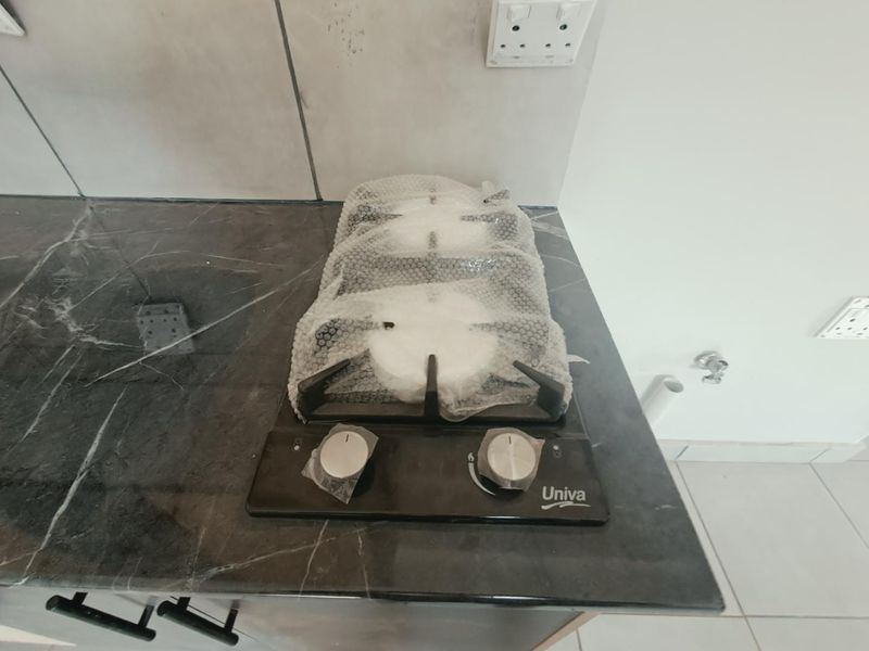 A close-up view of a new, unused gas hob installed on a dark marble-effect kitchen countertop with a tiled backsplash.