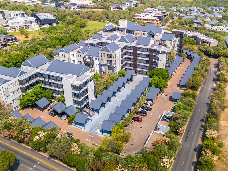 Aerial view of a modern apartment complex featuring multiple residential buildings, extensive covered parking facilities, and landscaped surroundings.