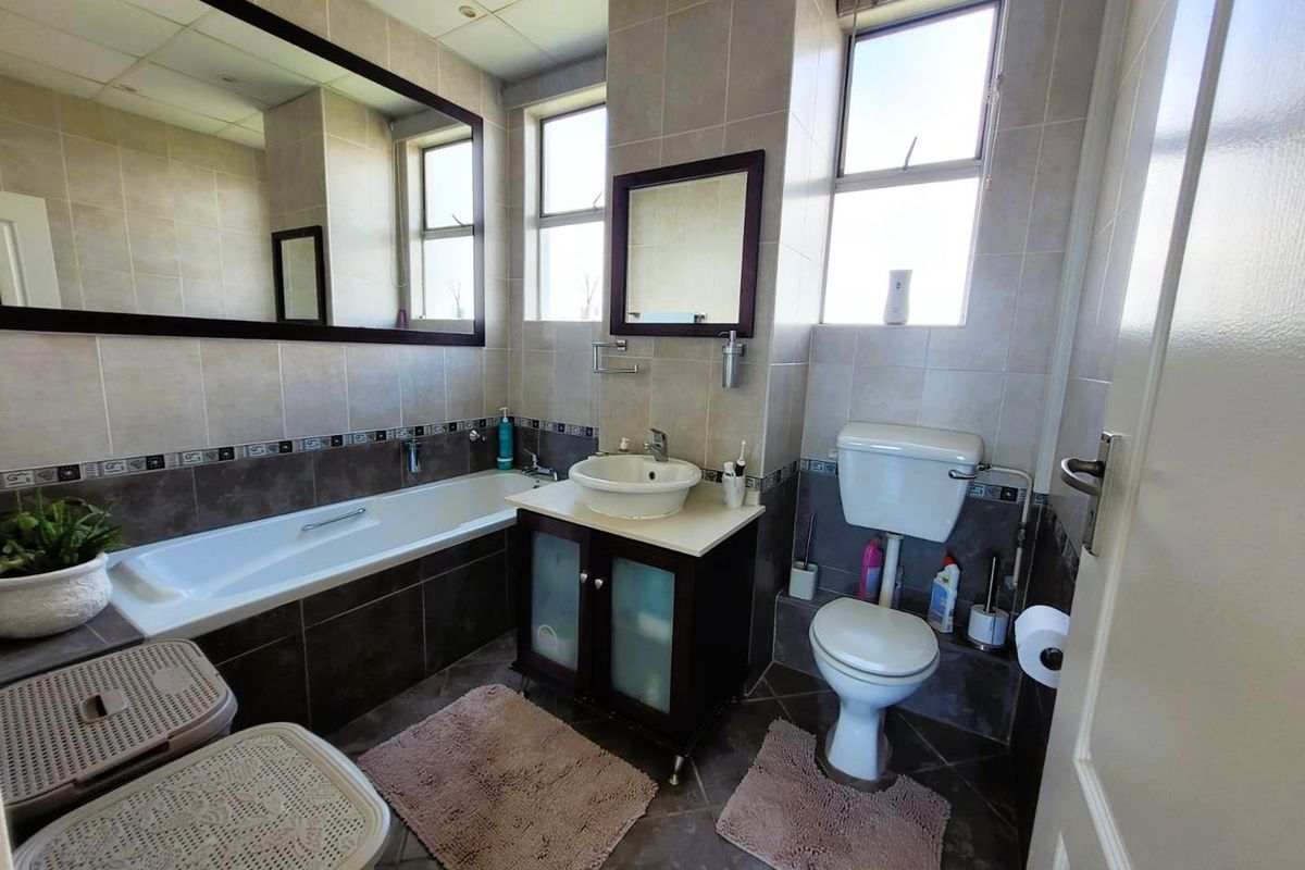 A functional bathroom featuring a built-in bathtub, a vessel sink vanity, and a standard toilet with neutral wall and floor tiling.