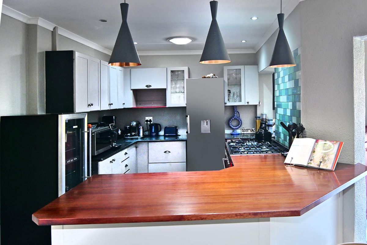 Modern kitchen featuring white cabinetry, a timber breakfast bar, gas hob, and stylish pendant lighting, creating a functional and inviting culinary space.