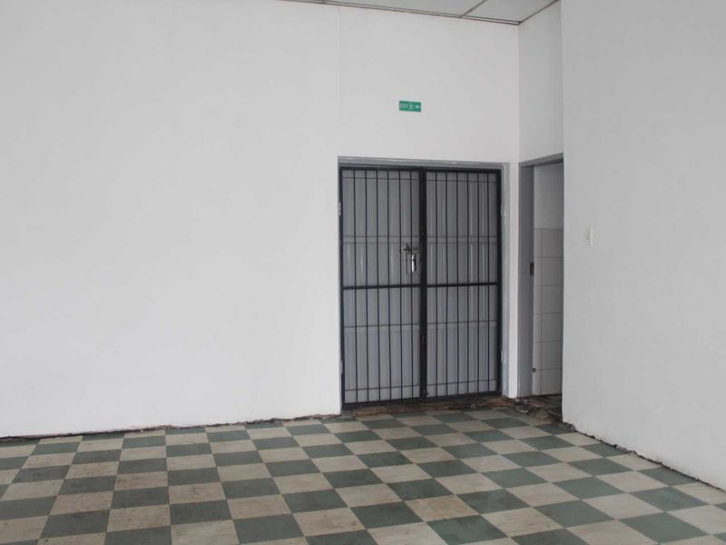 An empty retail space featuring checkered tile flooring, a security gate, and a suspended ceiling, suitable for various commercial business applications.