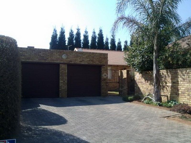 Front exterior view of the townhouse featuring a double garage, paved driveway, and secure gated entrance.