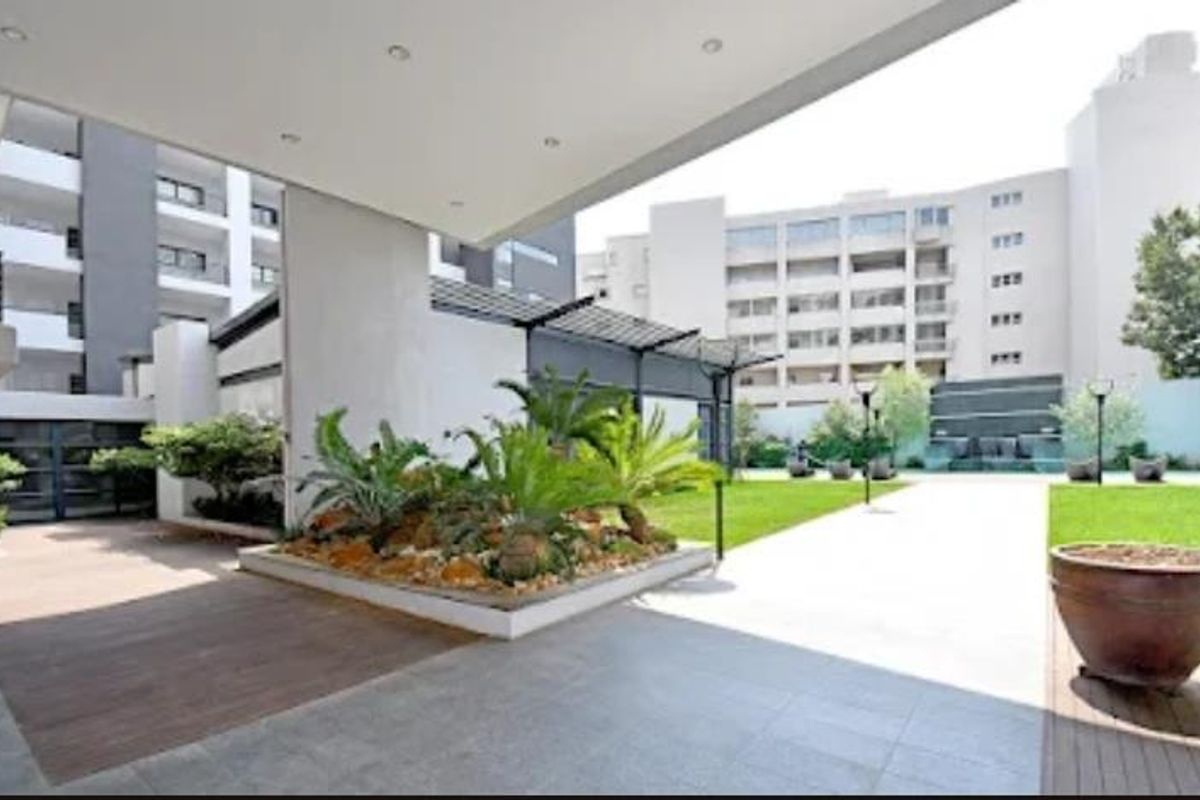 A well-maintained outdoor courtyard area featuring paved walkways, landscaped garden beds, and a covered patio space within an apartment complex.