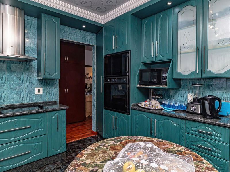A kitchen featuring teal-toned cabinetry, granite countertops, built-in oven and microwave, and a tiled backsplash with a decorative coved ceiling.
