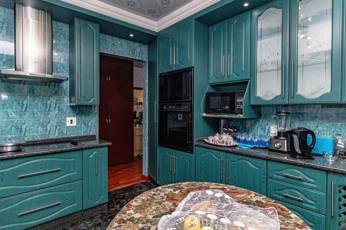 A kitchen featuring teal-toned cabinetry, granite countertops, built-in oven and microwave, and a tiled backsplash with a decorative coved ceiling.