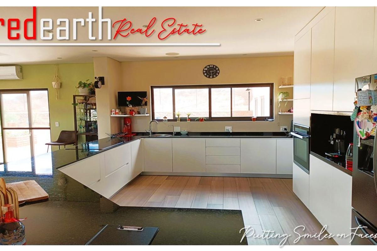 Modern open-plan kitchen featuring sleek white cabinetry, dark granite countertops, integrated oven, and large windows providing ample natural light.