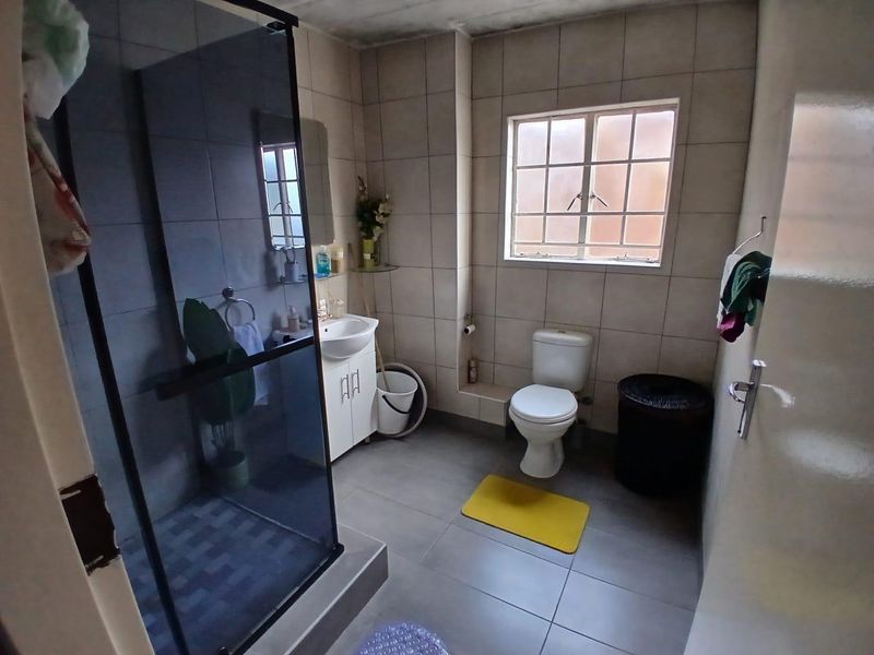 A functional bathroom featuring a shower enclosure, vanity cabinet with basin, and toilet, finished with neutral wall and floor tiles.