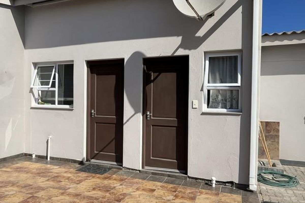 Exterior view of the rear facade featuring tiled patio flooring, two solid panel doors, and aluminium-framed windows with security bars.