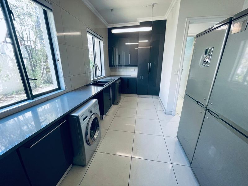 Modern laundry room featuring dark high-gloss cabinetry, stone countertops, an undermount sink, and large format floor tiles.