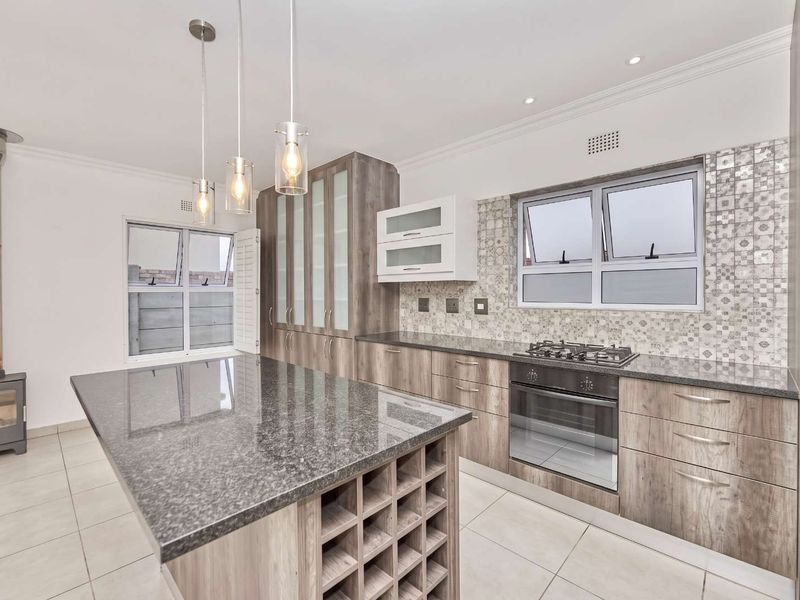 Modern kitchen featuring a large granite-topped island, built-in oven, gas hob, mosaic backsplash, and a contemporary wood-burning fireplace.