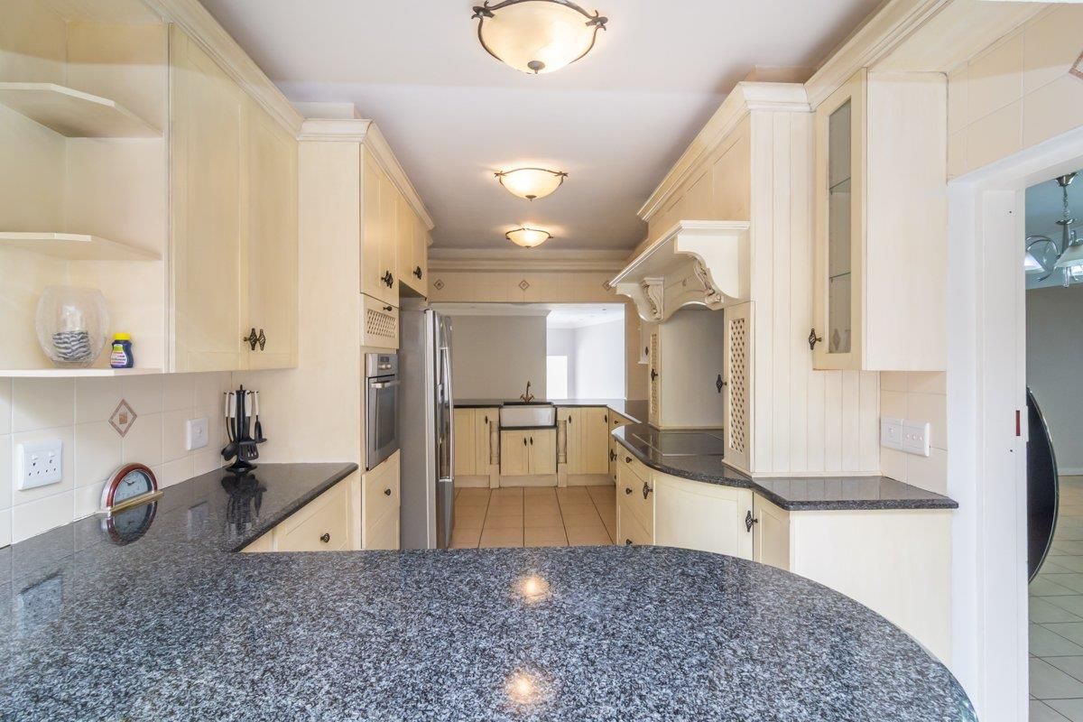 A traditional kitchen featuring cream cabinetry, dark granite countertops, a farmhouse-style sink, and built-in oven, offering a functional and classic layout.