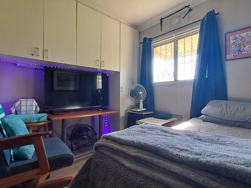 A functional bedroom featuring built-in cabinetry for storage and a window with security screening, providing natural light and ventilation.