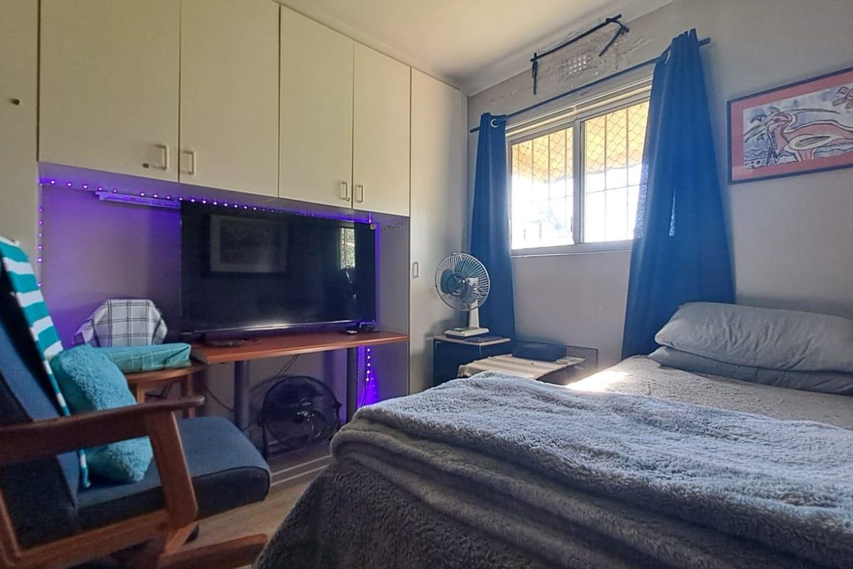 A functional bedroom featuring built-in cabinetry for storage and a window with security screening, providing natural light and ventilation.