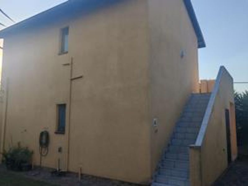 Rear view of a two-story residential building featuring a plastered facade and an external staircase leading to the upper level.