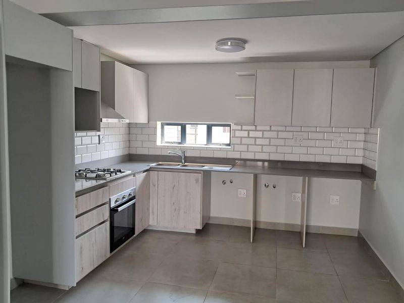 Modern kitchen featuring light wood-finish cabinetry, subway tile backsplash, gas hob, electric oven, and ample counter space with dedicated plumbing for appliances.