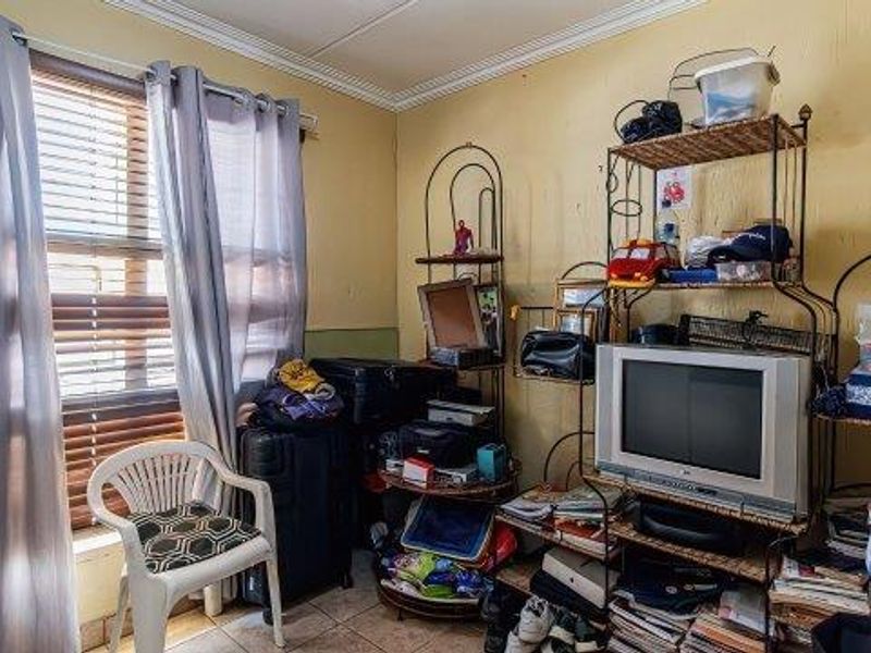 A bedroom featuring tiled flooring, venetian blinds, and crown molding, currently showing signs of wear including cracked plaster and peeling paint.