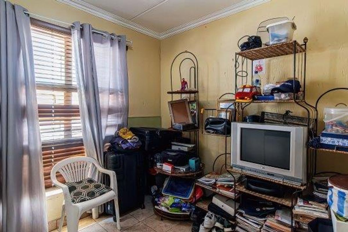 A bedroom featuring tiled flooring, venetian blinds, and crown molding, currently showing signs of wear including cracked plaster and peeling paint.