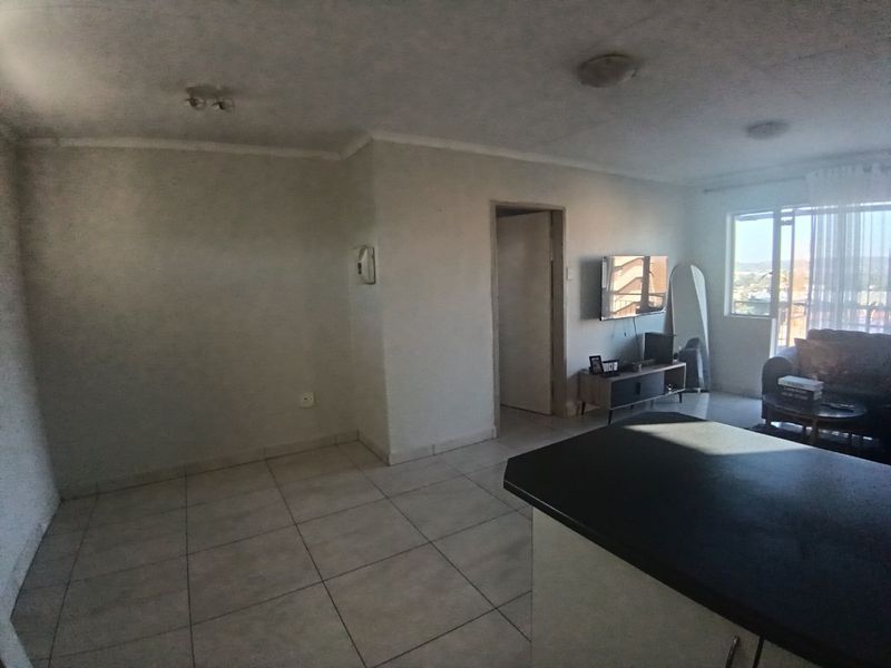 Open plan living area featuring tiled flooring and a kitchen island, providing a functional space with access to an adjoining room and balcony.