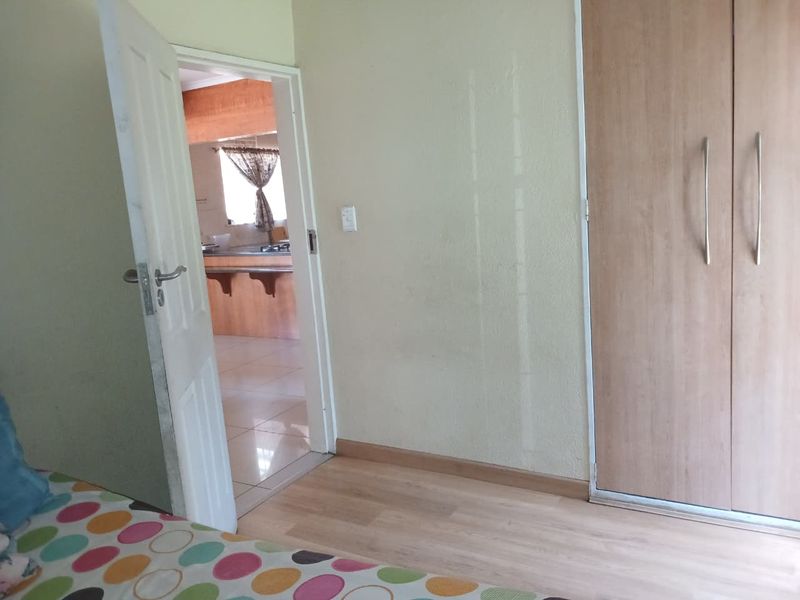 A bedroom featuring laminate flooring and a built-in wardrobe, with a view through the doorway into the adjacent kitchen area.